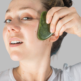 Person using a green jade roller on their face against a blue background